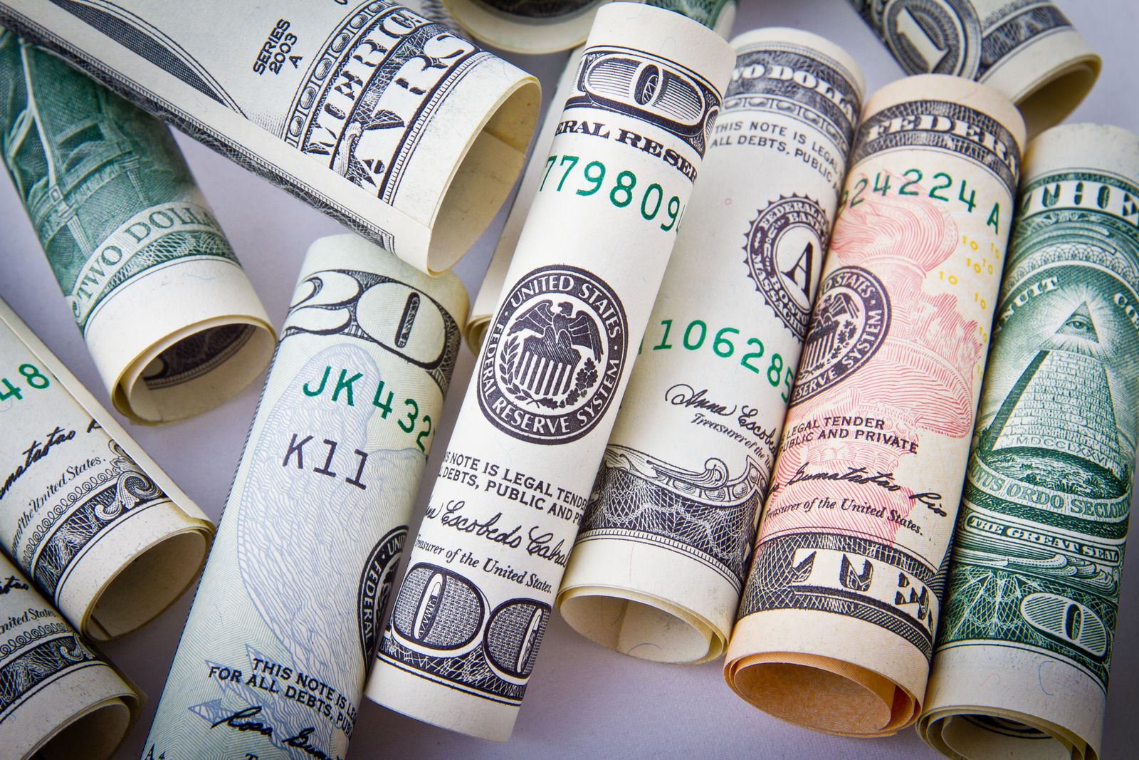 Rolled United States dollar bills of several denominations lying on a pale surface